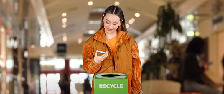 Image of girl in jacket putting an old phone in the mobilemuster recycling bin